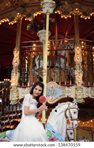 Beautiful delicate bride smiling in a carousel on her wedding day in Paris