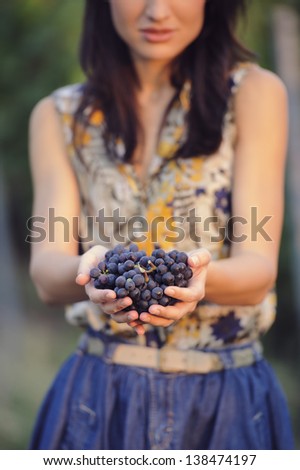 Beautiful delicate girl on a photo session in a vineyard, holding some grapes