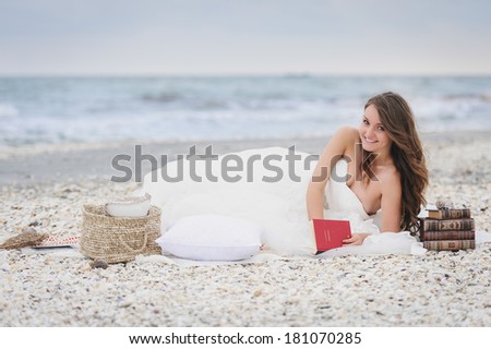 Beautiful bride reading on a beach surrounded by shells