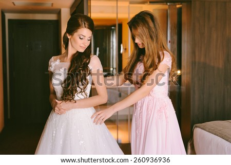Beautiful bride getting dressed by her best friend in her wedding day