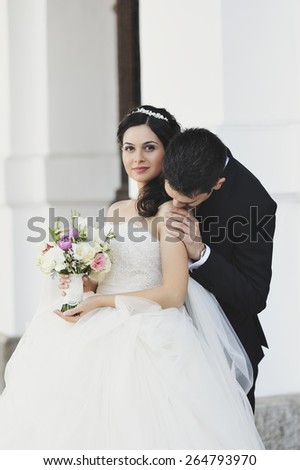 Beautiful, perfect couple posing on their wedding day. The groom is kissing his bride on the shoulder