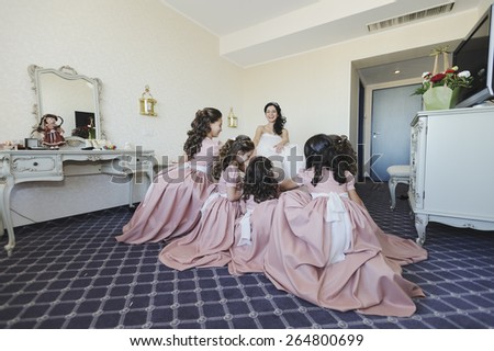Beautiful, stunning bride, getting dressed in her wedding day by some pretty little girls dressed in pink