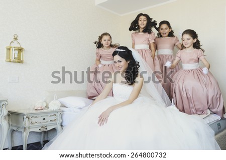 Beautiful, stunning bride, getting dressed in her wedding day by some pretty little girls dressed in pink