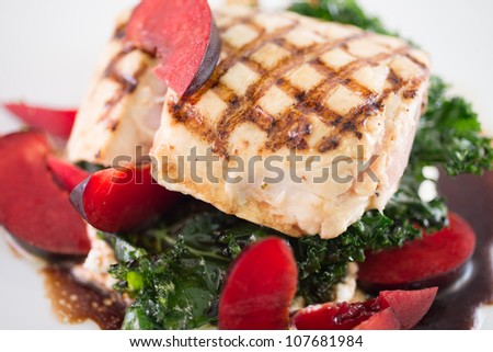 A gourmet healthy dinner of barbecued white sea bass atop a bed of kale and ricotta cheese dressed with fresh plums and balsamic vinaigrette.