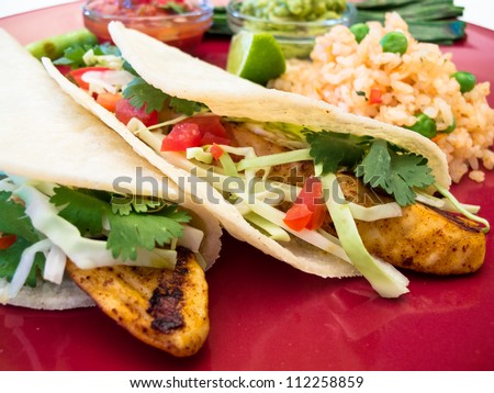 Fish Tacos with Guacamole and Rice: Seasoned grilled fish tacos in corn tortillas with salsa, cabbage, guacamole, lime, and rice.
