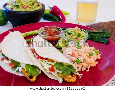 Fish Tacos with Guacamole and Rice: Seasoned grilled fish tacos in corn tortillas with salsa, cabbage, guacamole, lime, rice, and beer.
