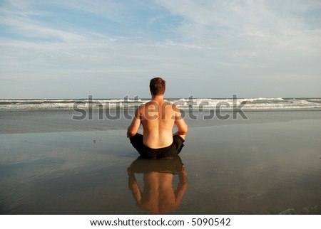 Man meditating on beach with reflection from sand