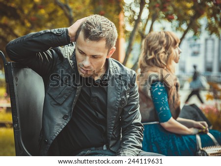 Sad young couple sitting on the bench after a quarrel