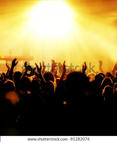 silhouettes of concert crowd in front of bright yellow stage lights