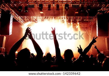 Rock concert, silhouettes of happy people raising up hands