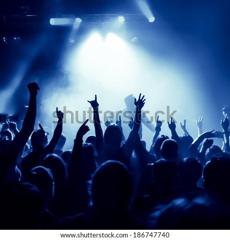 silhouettes of concert crowd in front of bright stage lights, singer on stage