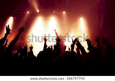 silhouettes of concert crowd in front of bright stage lights, singer on stage