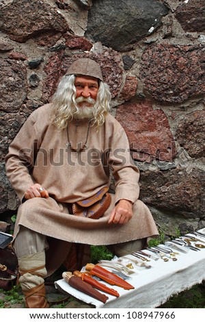 Old man in medieval clothes  is selling his blacksmith crafts