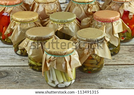 Jars with pickled vegetables arranged in order of bowling pins on wooden shelf against stone wall