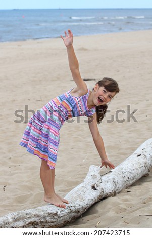 Cheerful girl stands on log and tries to keep balance outdoor