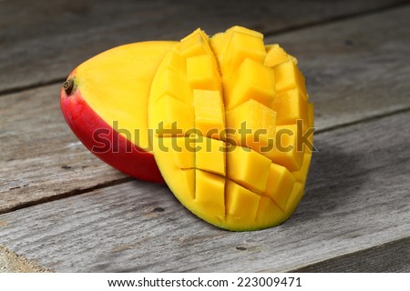 Two halves of ripe red mango fruit prepared for eating lie on wooden table closeup