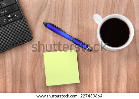Yellow scratch paper lies on desktop beside cup of coffee, pen and fragment of personal computer