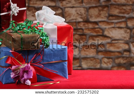 Christmas, New Year or other holiday decorative gift boxes pile on table on blurred stone wall background with copy space on the right side. Blank for greeting postcard