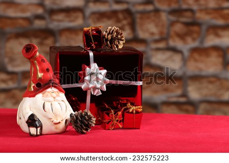 Santa figurine, decorative gift box and pine cones on red table on blurred stone wall background with copy space on right side. Blank for Christmas or New Year postcard