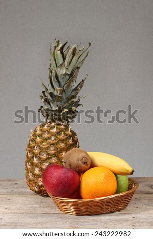 Set of exotic tropical fruits in basket with big pineapple on background lie on wooden table