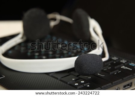 Headset on laptop - Black and white headphones with microphone lie on keyboard close up