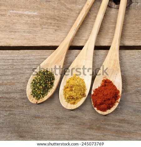 Green, yellow and red spice powder in long wooden spoons close up on rough country table