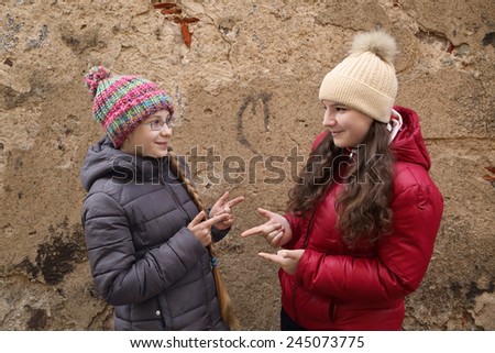 Two teenage girls in winter clothes outdoor play rock, paper, scissors (roshambo) on old grunge wall background