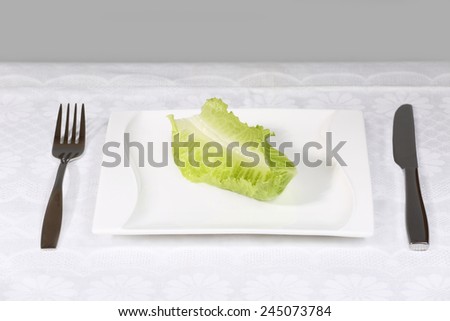 Diet, weight loss, low calories food concept - single green salad leaf on plate with fork and knife on the table
