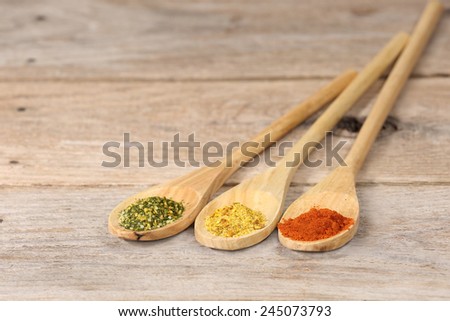 Green, yellow and red spice powder in long wooden spoons on rough country table