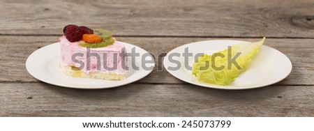Diet, weight loss, low calories food concept - choice between pleasure and healthy lifestyle - plates with delicious sweet cake and single green salad leaf on the wooden table