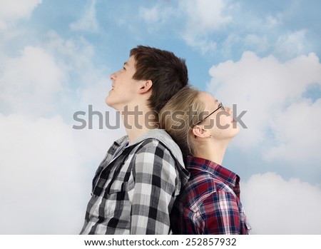Teenage relationship and friendship - Boy and girl in plaid shirts stand back to back and looking thoughtfully into the cloudy blue sky