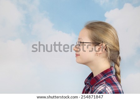 Pretty teenage girl looks ahead on cloudy blue sky background - romantic youth concept