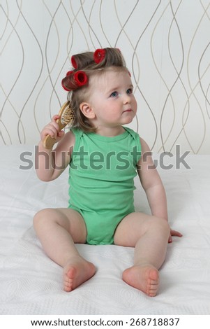 Beauty and style from early childhood - Infant baby with with hair curlers and hairbrush makes hairstyle sitting on sofa