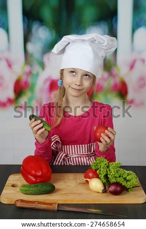 Pretty little girl in white chef hat cooks vegetarian salad
