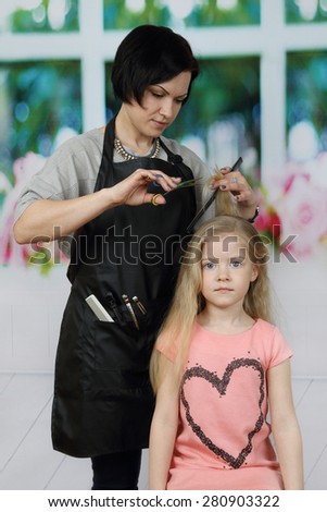 Brunette woman hairdresser cuts little blonde girl long hair