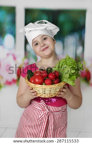Little round faced girl in chief hat with basket of vegetables in hands