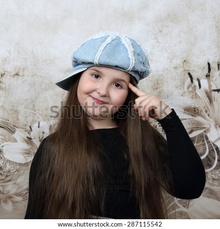 Cute long haired plump round faced girl in cap puts index finger to her temple