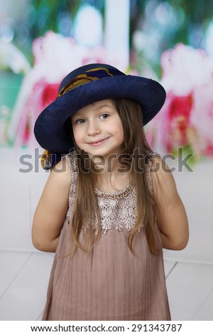 Cute little girl in too big hat hides hands behind back - surprise or secret, does not want to show