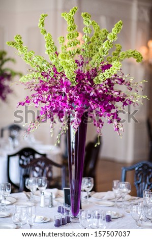 Purple orchid floral centerpiece highlights a formally set table at a wedding reception.