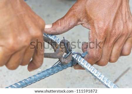hands of builder worker use pincers and wires for knitting metal rods at the construction site