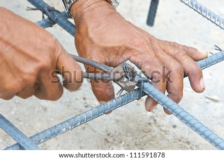 hands of builder worker use pincers and wires for knitting metal rods at the construction site