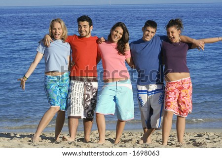 Five friends in different coloured t-shirts,goofing about at beach