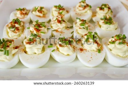 Plate of fancy devilled eggs, topped with chives and paprika.  Delicious food for a lunch, appetizer, or afternoon tea.