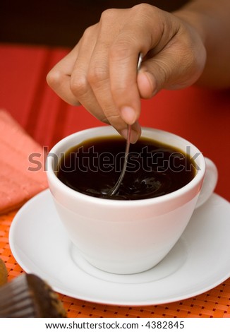 Stirring black coffee in a white cup and saucer
