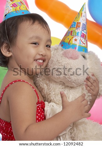 young girl holding teddy bear with party hat