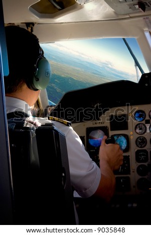 Pilot in the cockpit of a small commercial aircraft above a rural landscape.