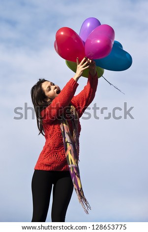 cheerful girl with heart shape balloons against blue sky background