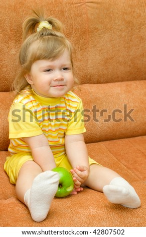 Little smiling girl in yellow eat green apple