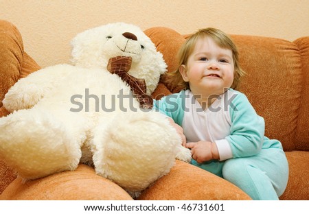 Small baby sitting in armchair with toy bear