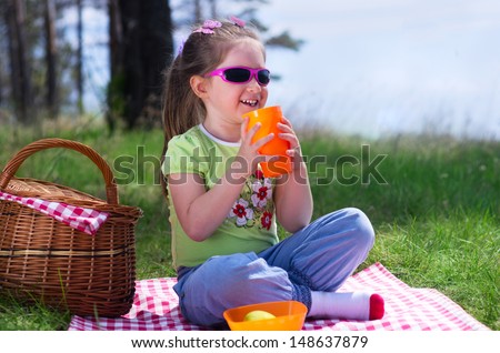 Little girl with plastic cup and picnic basket at forest